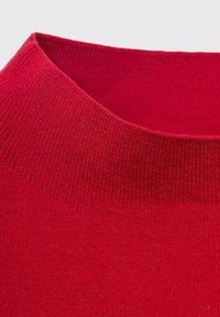 Gros plan sur le col d'un pull en tricot côtelé rouge avec un col rond, sur un fond neutre.