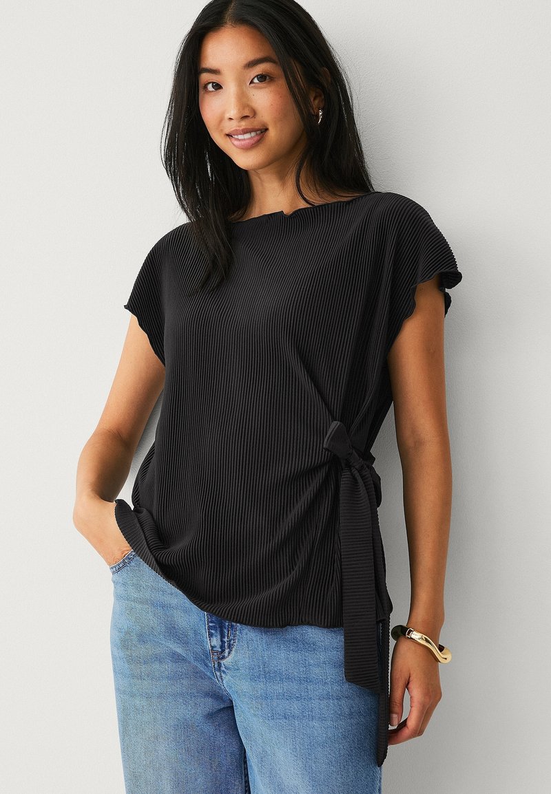 Sort plisseret top med korte ærmer og en sidebinding, parret med lyseblå jeans. Glat tekstur med en afslappet pasform.