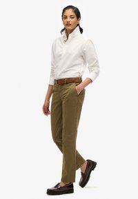 Chemise blanche à manches longues avec boutons, chinos verts olive et mocassins marron foncé. Ceinture en cuir marron assortie aux accents des chaussures. Texture de tissu lisse.