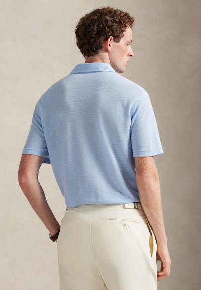 Ανοιχτό μπλε πόλο μπλούζα με κοντά μανίκια και υφή, με κλασικό γιακά και χαλαρή εφαρμογή, σε συνδυασμό με μπεζ παντελόνια.