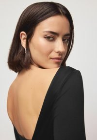 Sort langærmet beklædning med dyb V-ryg, glat tekstur og tætsiddende silhuet. Indeholder subtile designdetaljer og minimalistisk stil.