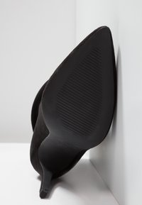 Chaussure à talon haut en daim noir avec un bout pointu et un talon aiguille fin. Semelle en caoutchouc texturé avec des rainures horizontales pour une meilleure adhérence.