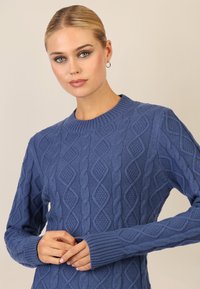 Maglione azzurro lavorato a maglia con un motivo a rombi in rilievo, polsini a costine e scollatura rotonda. Il filato morbido e spesso aggiunge profondità.