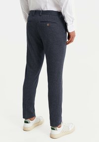 Námořnické modré kalhoty vyrobené z texturované tkaniny, s úzkým střihem, dvěma zadními kapsami s knoflíky a nošené s bílými teniskami.