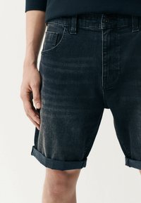 Jeansshorts in dunkler Waschung mit leicht abgewetzter Textur, ausgestattet mit umgeschlagenen Säumen, einer Vordertasche und einem sicheren Knopfverschluss.