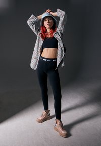 Leggings sportive negre cu logo alb Nike, completate cu un top scurt negru. Outifit-ul este completat de un sacou oversized cu carouri și adidași bej.