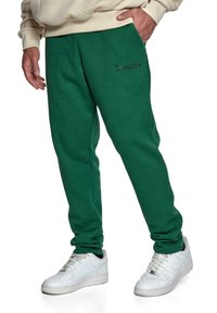 Grønne sweatpants med en blød tekstur og et broderet "Dropsie" logo i mørkegrå. Kombineret med hvide sneakers.