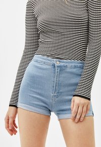 Höga denimshorts i ljusblått, med uppvikta fållar, fem fickor och knappstängning fram. Horisontell topp med svartvita ränder.