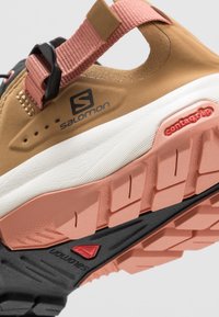 Scarpa da trail Salomon con tomaia beige, accenti rosa e suola multistrato nera e rosa con logo Contagrip.