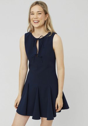 Robe sans manches bleu marine avec un décolleté en forme de clé et un détail à nouer, présentant une jupe évasée, un design plissé et une texture de tissu lisse.