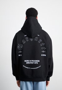 Felpa nera con cappuccio ampio, caratterizzata da scritte bianche e dettagli grafici sul retro. Materiale morbido con vestibilità comoda.