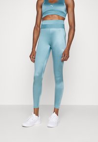 Crop top de sport bleu clair et leggings taille haute assortis en matériau lisse et brillant. Accent logo blanc sur les deux pièces. Baskets blanches.