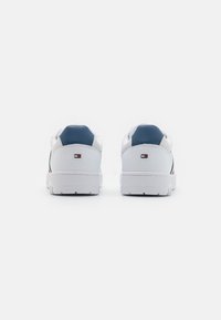 Białe sneakersy z gładką skórzaną cholewką, granatowymi akcentami, szczegółami w czerwono-granatowe paski i teksturowaną gumową podeszwą.