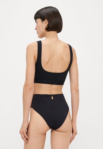 Top curto preto com alças largas e costas baixas, combinado com cuecas de biquíni de cintura alta. O material parece suave com um brilho subtil e detalhe em forma de abertura.