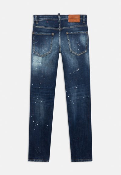 Tummansiniset farkut kuluneella ilmeellä, joissa valkoisia ja punaisia maalitahroja, viisi taskua ja nahkainen merkkilaatta vyötäröllä.