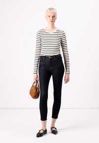 Sötétkék skinny farmernadrág csíkos, hosszú ujjú felsővel párosítva, fekete, tüskés lapos cipővel és egy kis barna kézitáskával. Simább textúrák és testhezálló dizájn.
