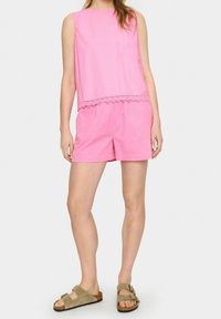 Haut sans manches rose avec un bord en dentelle festonnée, assorti à un short rose. Porté avec des sandales beiges à double boucles réglables.