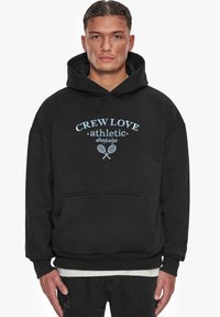 Svart hettegenser laget av bomull, med en frontlomme, ribbestrikkede mansjetter, og et grafisk trykk i lys blå som leser "CREW LOVE athletic."