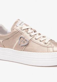 Metallic beige sneakers with a white platform sole, featuring a heart-shaped metal accent and flat laces, crafted from smooth fabric.