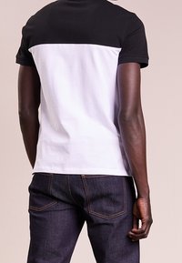 T-shirt med kort ärm med en svart övre del och en vit nedre del, gjord av bomull, med rundad halsringning och avslappnad passform.