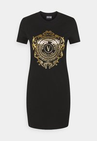 Černé krátké šaty s krátkým rukávem, zlatým zdobeným kruhovým emblémem a nápisem "Versace Jeans Couture" uprostřed na hrudi.