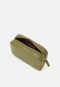 Prostokątna torebka z teksturowanej oliwkowej skóry, z złotym zamkiem błyskawicznym, częściowo otwarta, odsłaniająca ciemne wnętrze i małą metkę marki w środku.