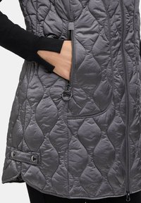 Kurtkę pikowaną w kolorze szarym z zamkiem błyskawicznym, ukrytymi kieszeniami po bokach i ściągaczem z zatrzaskami na dole. Gładka tekstura z wzorem diamentowym.