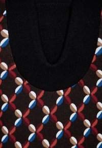 Encolure côtelée noire avec un tissu à motifs en dessous présentant des formes florales multicolores en rouge, bleu, blanc et marron sur un fond sombre.