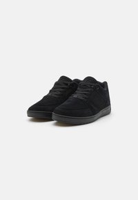 Black suede low-top sneakers with lace-up closure, cushioning around the ankle, and a black rubber sole. Textured accents on the upper.