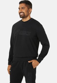 Sweatshirt noir avec un col rond, mettant en avant un grand logo en relief "ASICS" sur le devant. Le matériau semble lisse et tricoté.