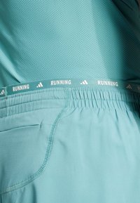 Ljusblå löparshorts med meshstruktur, elastisk midja med texten "RUNNING" och sidofickor.