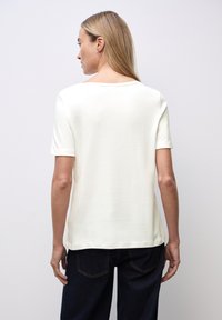 Kortærmet cremefarvet t-shirt, blødt bomuldsstof, rund halsudskæring, lidt afslappet pasform, kombineret med mørk denim bukser, ren afslutning.