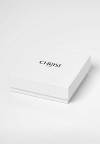 Weißer rechteckiger Schmuckkasten mit schwarzem "CHRIST seit 1863"-Text, der in der Mitte des Deckels platziert ist, auf einer weißen Oberfläche.