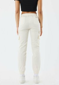 Cremefarbene Cargo-Hosen mit elastischem Bund und Bündchen. Mit seitlichen Cargo-Taschen und zwei Gesäßtaschen, aus weichem, strapazierfähigem Stoff gefertigt.