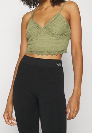 Olivgrön spetscroptop med smala axelband, med strukturerade mönster och vågig fåll, kombinerad med svarta högmidjade leggings.