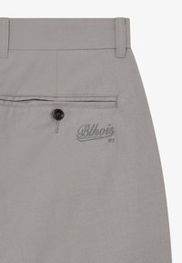 Graue Hose aus strukturiertem Stoff, mit einer Gesäßtasche mit einem schwarzen Knopf und gesticktem "Blkwois NY"-Logo.