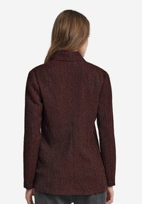 Burgundy-texturerad kavaj med krage, långa ärmar och skräddarsydd passform. Synliga sömdetaljer längs sömmarna och baksidan.