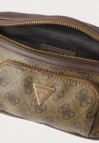 Barna szintetikus kézitáska, melynek felületén dombornyomott logóminta található. Arany cipzár záródással, barna bőrszegéllyel és aranyszínű fémalkatrészekkel.