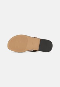 Sole di sandalo sintetica marrone con superficie testurizzata e accentuazione nera sul tacco; presenta un design piatto per un comfort durante l'uso.