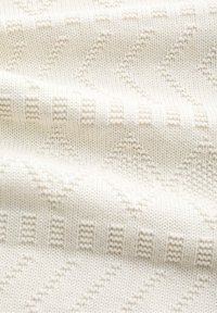 Tekstura kremastog pletenog materijala s suptilnim cik-cak uzorkom. Materijal izgleda mekano i lagano, prikazujući finu, glatku teksturu.