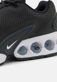 Crne Nike tenisice s teksturiranim gornjim dijelom, siva naglasna mjesta, zaobljeni bijeli potplat i vidljive zračne mjehuriće. Šnjalice i logo u kontrastnoj bijeloj boji.
