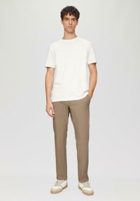 Biała bawełniana koszulka z okrągłym dekoltem zestawiona z jasnobrązowymi spodniami i beżowymi sneakersami z białymi i brązowymi akcentami. Prosty, codzienny styl.