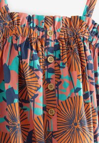 Robe sans manches en tissu léger avec un motif floral rose, bleu et orange. Elle présente un corsage froncé et des boutons en bois.