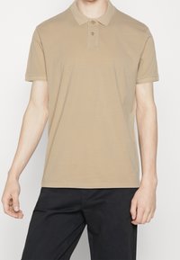 Polo beige avec un col classique, une patte de boutonnage à trois boutons et des manches courtes. Matière en coton douce avec une texture lisse.