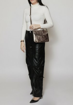 Borsa in bronzo metallico con chiusura a pattina e dettagli decorativi a strisce verticali. Indossata con un dolcevita bianco e pantaloni cargo in pelle nera.