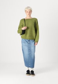 Zöld kötött, oversize pulóver, kék farmer maxi szoknya, fekete sportcipő és kis fekete táska. A pulóver bordázott mandzsettákkal és nyakkivágással rendelkezik.
