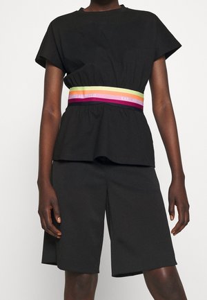 Persona che indossa un top nero a maniche corte e pantaloncini al ginocchio con una fascia elastica multicolore con l'etichetta Karl Lagerfeld.