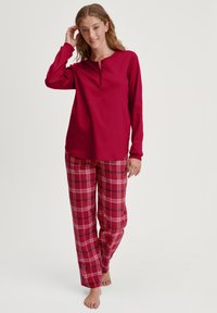 Langemouwen rode top met een henley-halslijn, gecombineerd met rode geruite pyjamabroek met witte en zwarte accenten. Casual, comfortabele ontwerp.