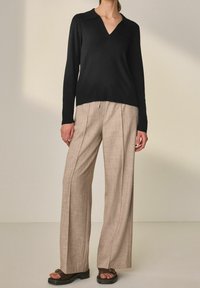 Maglione di maglia nera con scollatura a V e dettagli a coste, abbinato a pantaloni beige a gamba larga e texture, e sandali neri con plateau.
