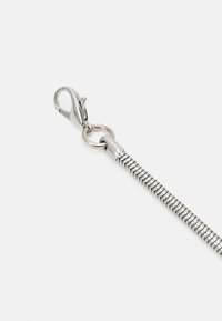 Collier chaîne serpent en argent avec fermoir mousquetaire sur fond uni gris clair.